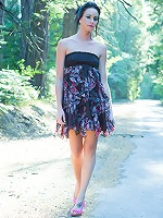 Justine Jewel playfully poses amidst the tall trees on a countryside road, lifting her dress' skirt to flash her smooth, pink pussy, in attempt to hitch a ride.